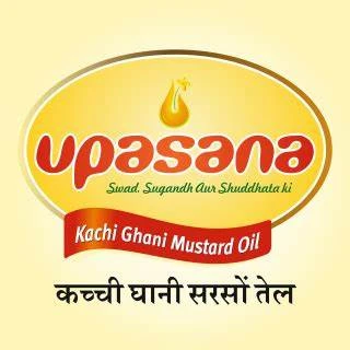"Upasana mustard oil logo featuring the brand name 'Upasana' in bold red lowercase letters with a mustard oil drop graphic above the letter 'p'. The background is an oval gradient of yellow and orange, with the tagline 'Swad, Sugandh Aur Shuddhata ki' in 